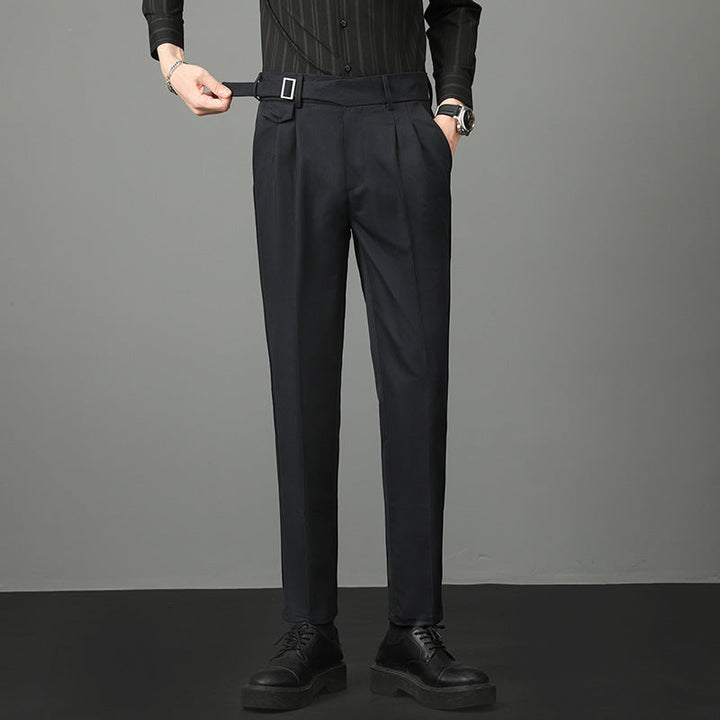 Pantaloni eleganti neri da uomo, con cintura e pieghe, abbinati a camicia nera e scarpe classiche. Moda maschile formale.