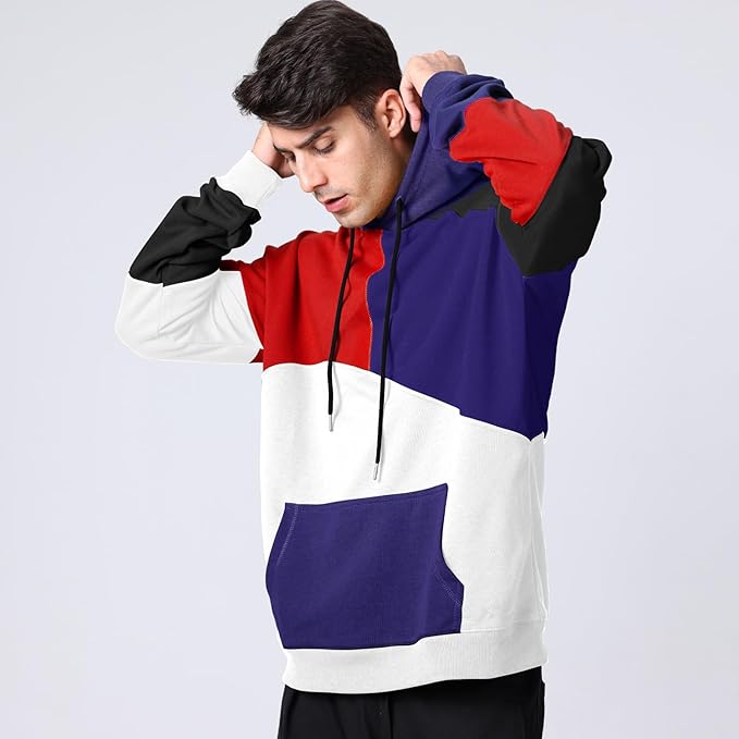 Giovane uomo con felpa multicolore a blocchi rosso, blu, nero e bianco, cappuccio alzato. Moda casual, abbigliamento streetwear moderno.