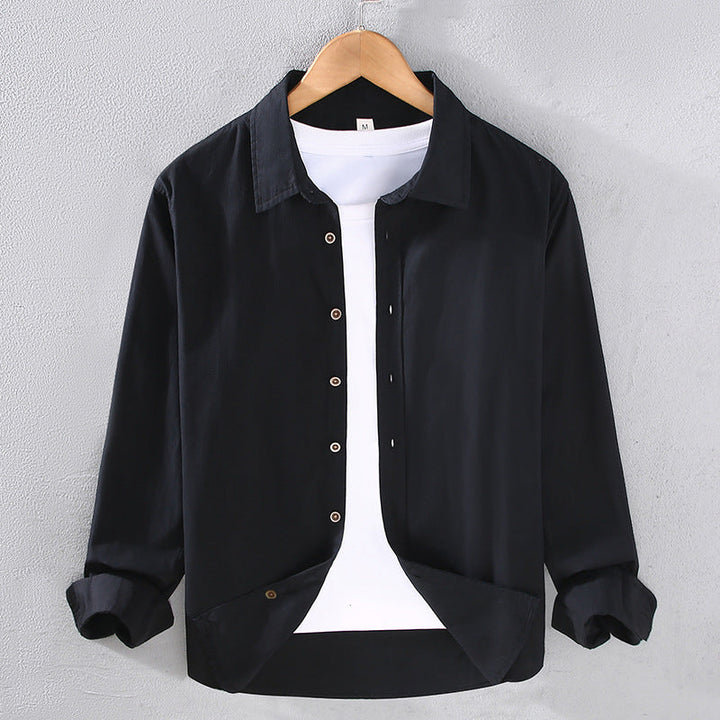 Camicia nera casual da uomo su gruccia, con bottoni e maniche lunghe, indossata sopra una maglietta bianca. Moda maschile elegante e moderna.