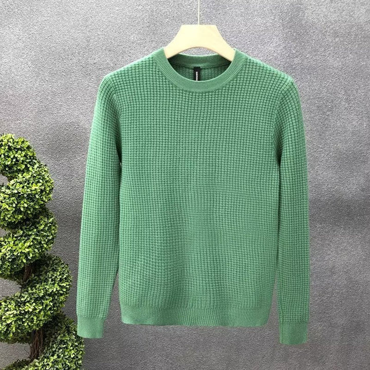 Maglione verde in maglia a trama grossa su appendiabiti, sfondo grigio. Moda uomo, abbigliamento invernale, stile casual elegante.