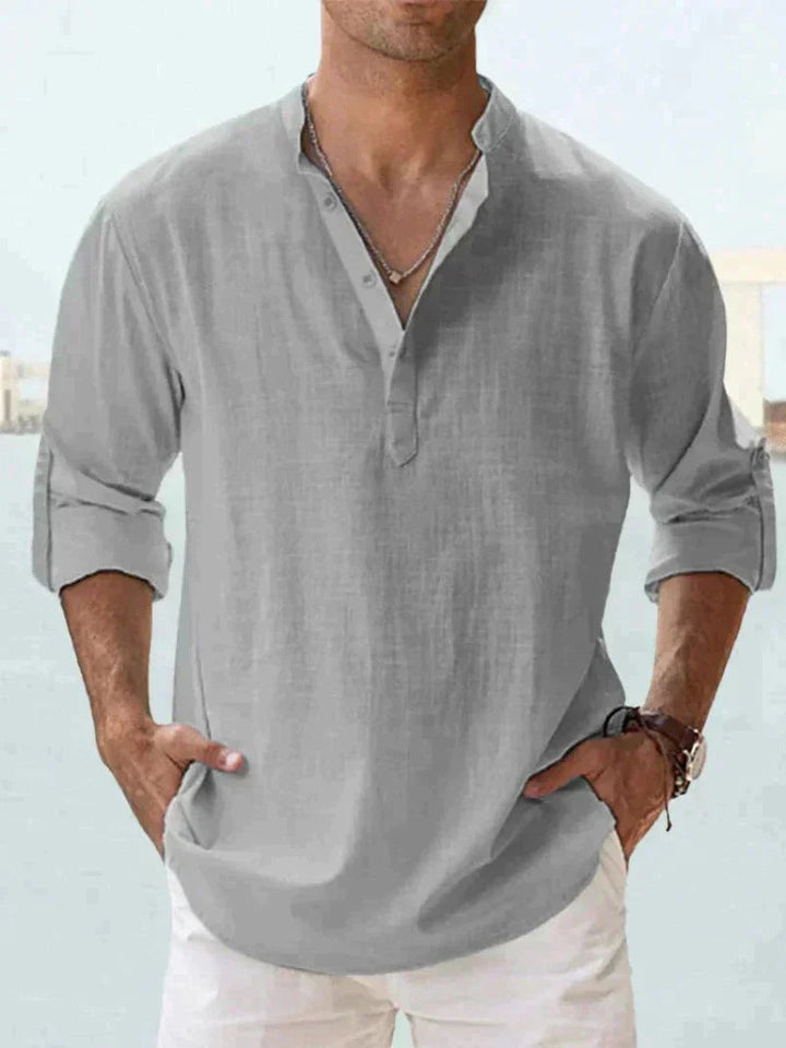 Camicia uomo lino grigia con colletto alla coreana, maniche lunghe arrotolate, abbinata a pantaloni bianchi. Stile casual elegante estivo.