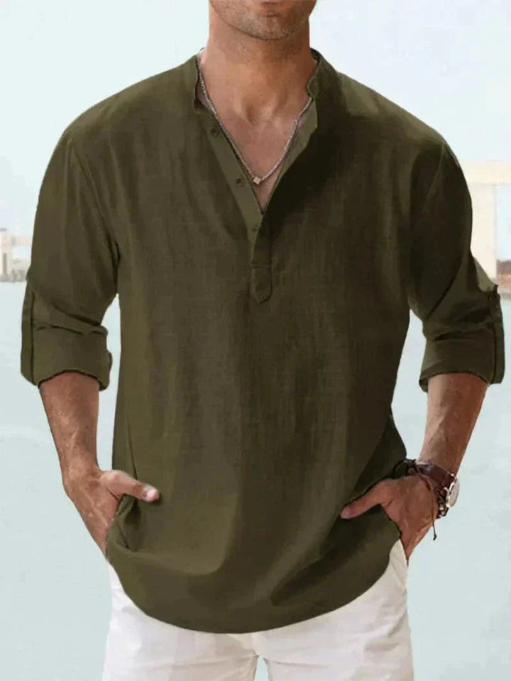 Camicia uomo verde oliva, maniche lunghe arrotolate, scollo a V con bottoni, stile casual, indossata con pantaloni bianchi.