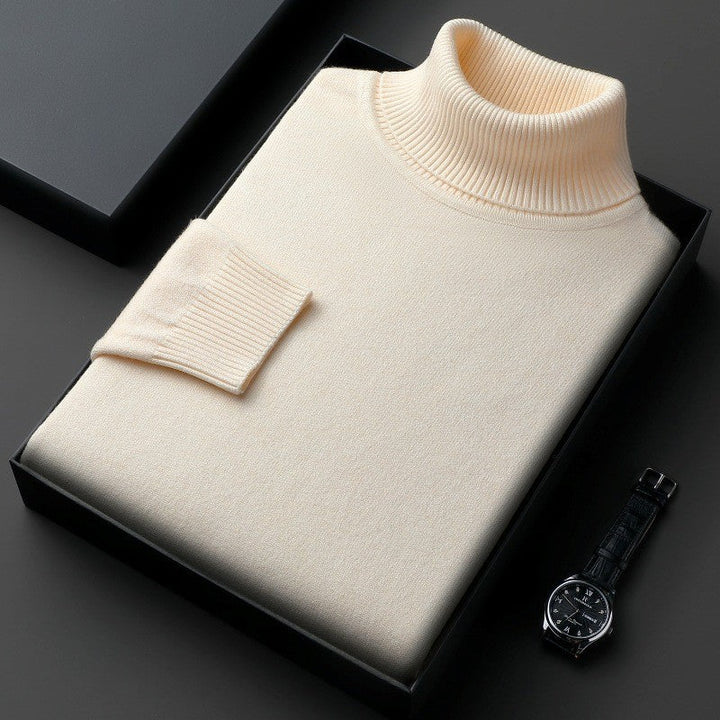 Maglione dolcevita beige in lana, confezionato in elegante scatola nera, accanto a orologio da polso nero su sfondo grigio scuro.