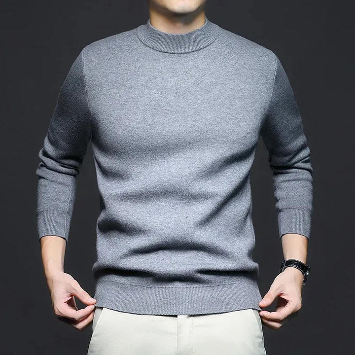 Maglione grigio uomo, maniche lunghe, collo alto, indossato su pantaloni chiari. Moda maschile elegante, abbigliamento casual autunnale.