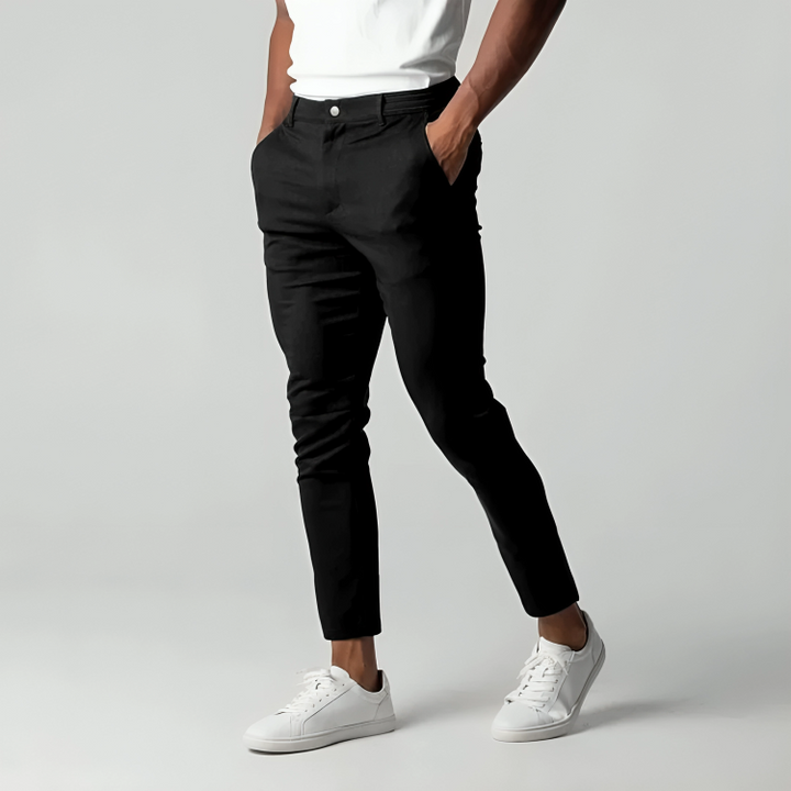 Uomo in pantaloni neri eleganti e scarpe da ginnastica bianche, posa su sfondo grigio. Moda maschile casual, stile moderno.