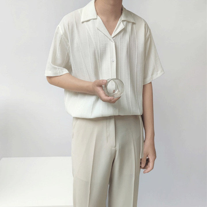 Uomo in camicia bianca e pantaloni beige tiene un bicchiere trasparente. Moda minimalista estiva, abbigliamento casual elegante.